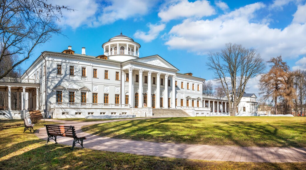 A large white building with columns and a dome, surrounded by a grassy area and trees.