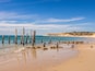A beach with wooden posts in the water and a sandy shore.