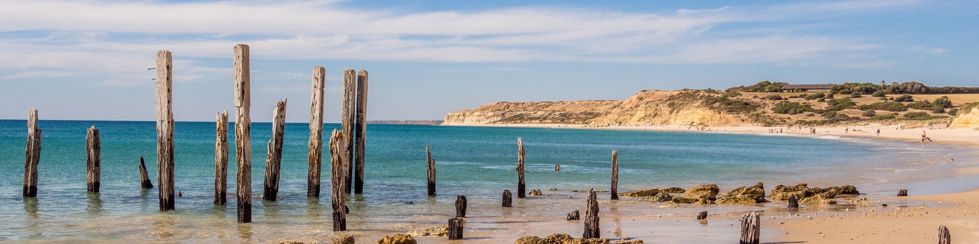 Una playa con postes de madera en el agua y una orilla arenosa.