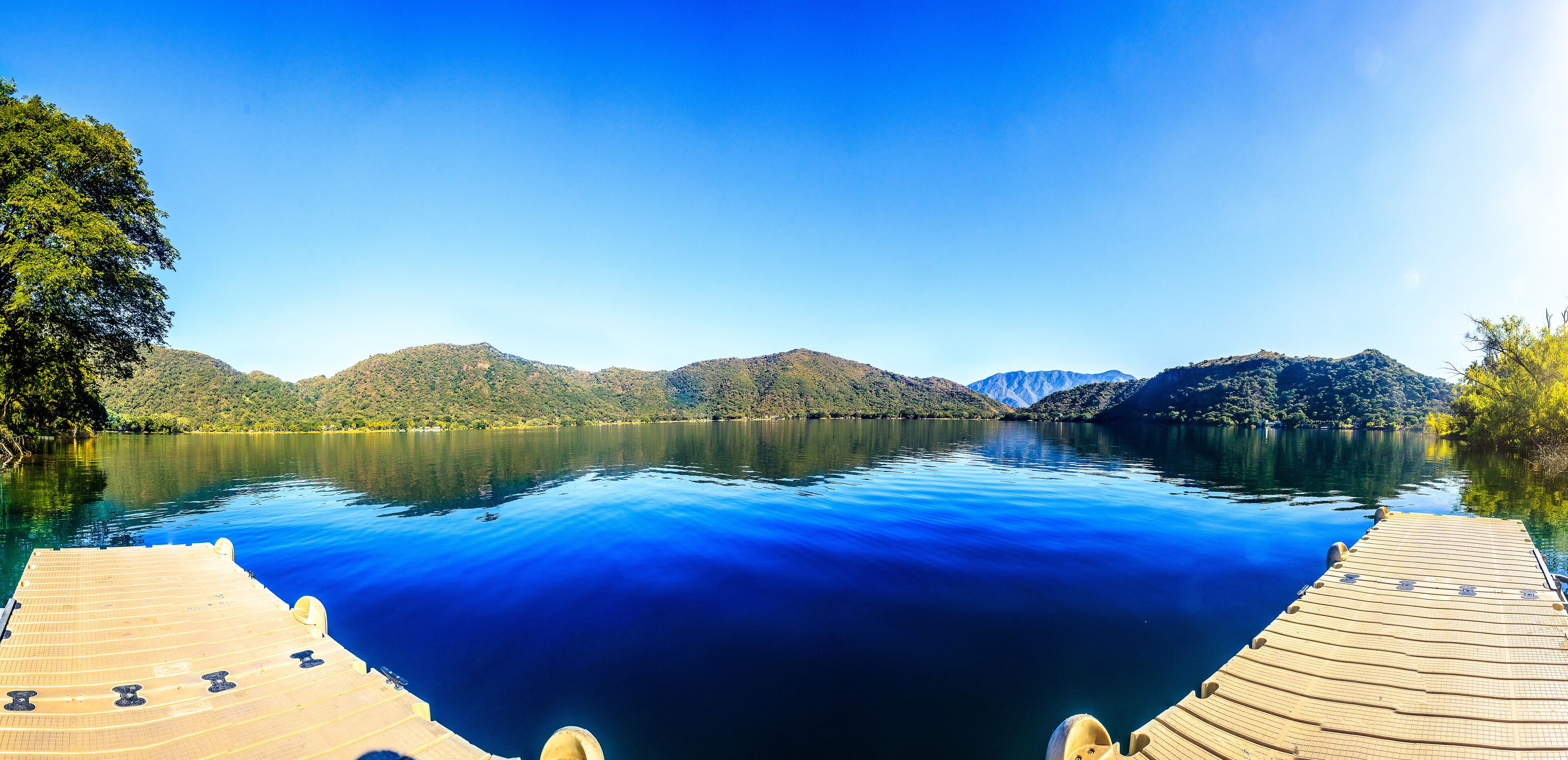 A calm lake with a wooden dock, surrounded by forested hills and mountains.
