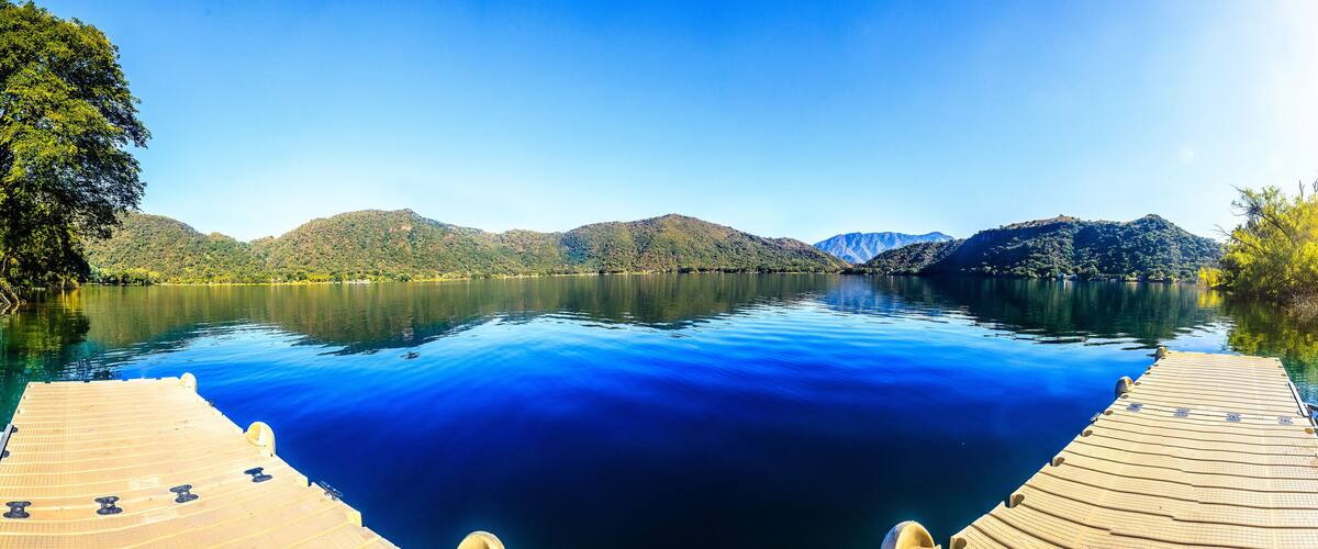 A calm lake with a wooden dock, surrounded by forested hills and mountains.