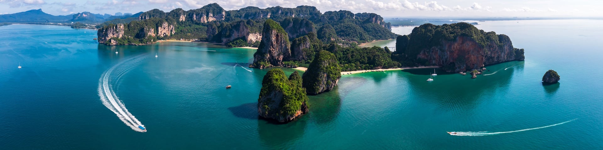 A coastal landscape with limestone karsts, clear turquoise waters, and boats.