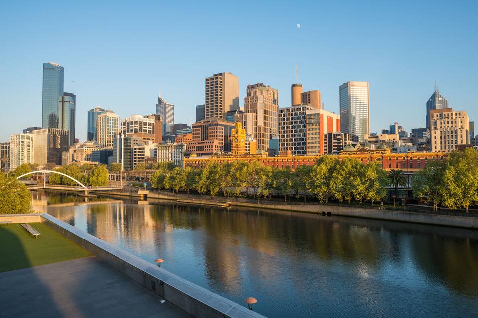 A city skyline with modern buildings, a river, and a bridge.