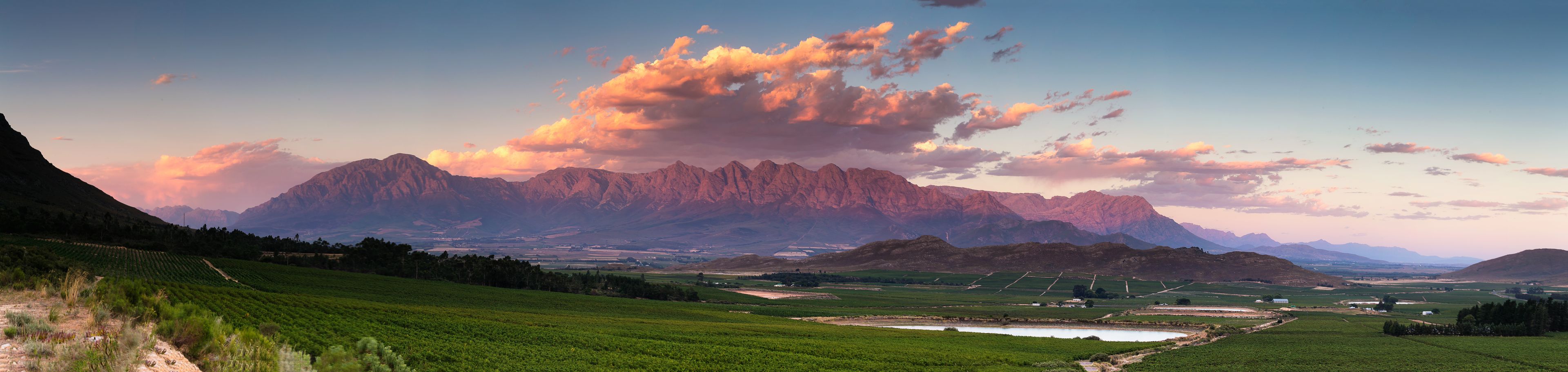 A mountainous landscape with a valley, green fields, and a small body of water.