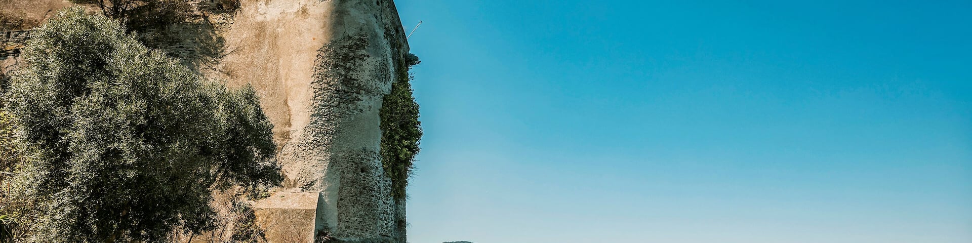 Un pueblo costero con una fortificación histórica, un cielo azul despejado y vistas al mar.