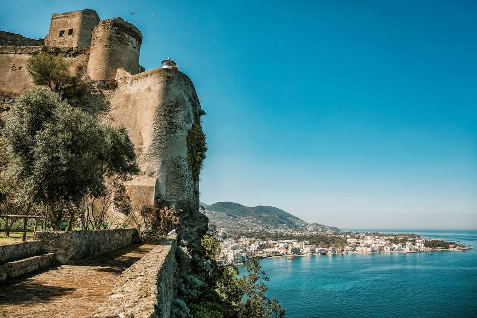 Un pueblo costero con una fortificación histórica, un cielo azul despejado y vistas al mar.
