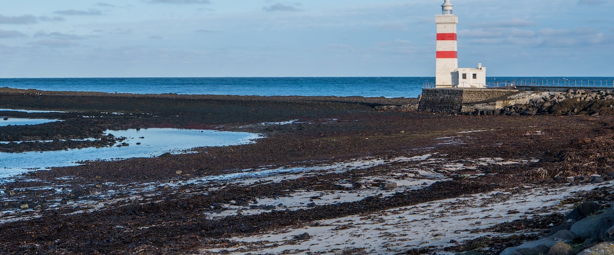 A lighthouse on a rocky shore with the sea in the background.