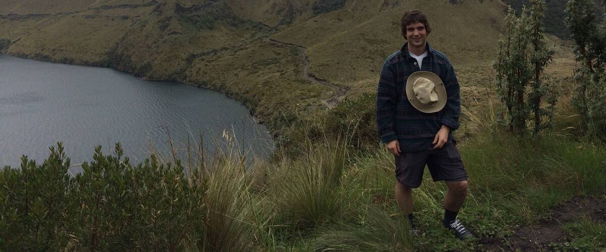 A person standing on a grassy hill overlooking a lake with mountains in the background.