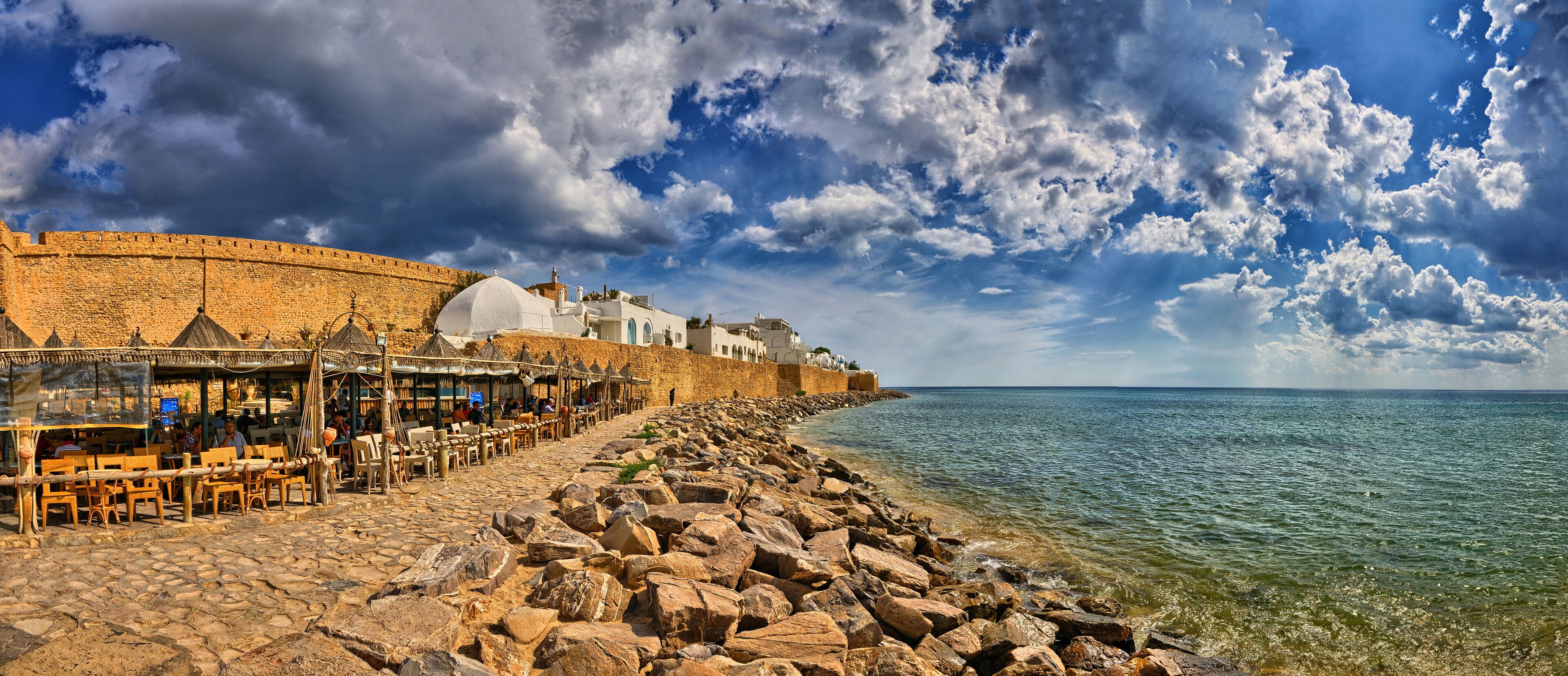 A coastal town with a stone wall, beachside café, and rocky shoreline.
