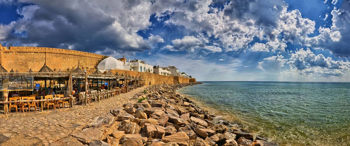 A coastal town with a stone wall, beachside café, and rocky shoreline.