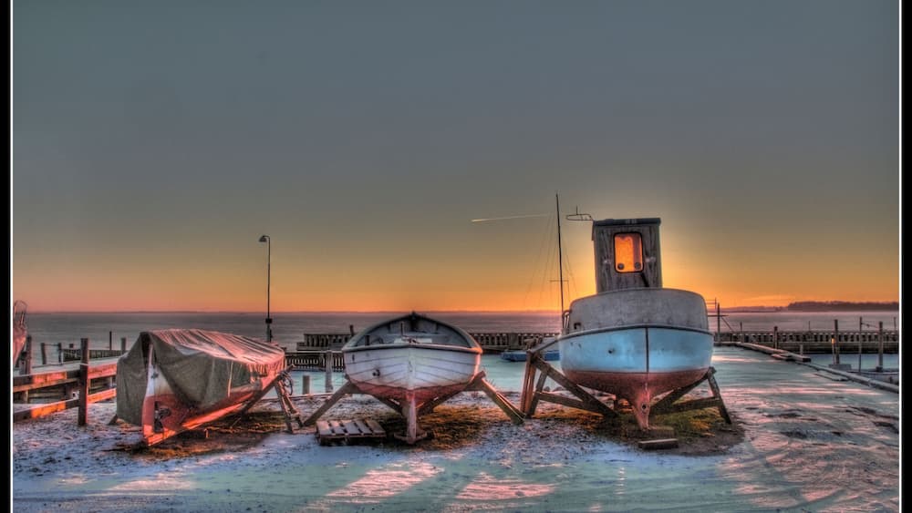 Trois bateaux sont amarrés à un quai, avec un coucher de soleil en arrière-plan.