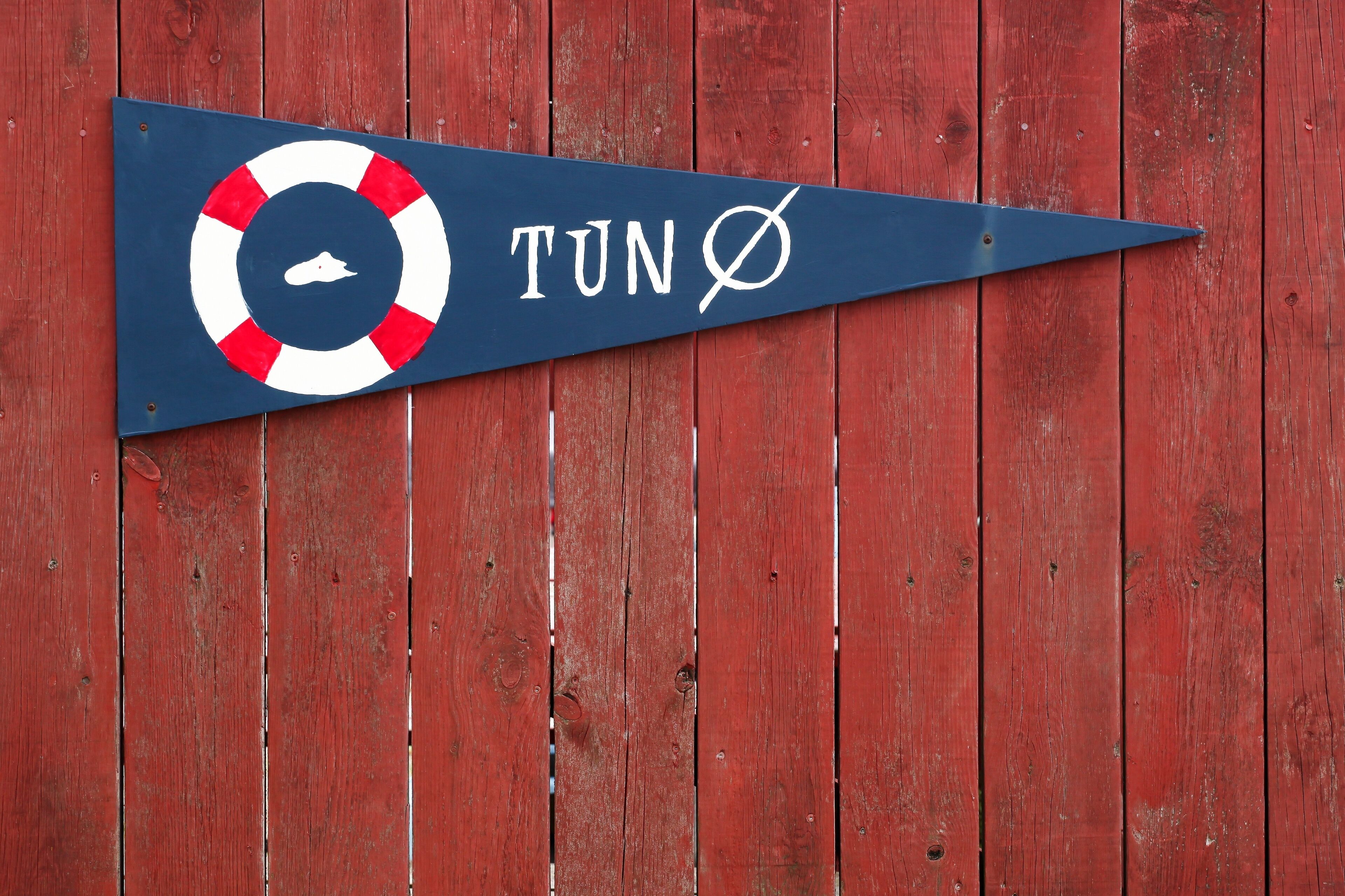 A directional sign with a lifebuoy symbol and the text "TUN Ø" on a blue background, mounted on a red wooden wall.