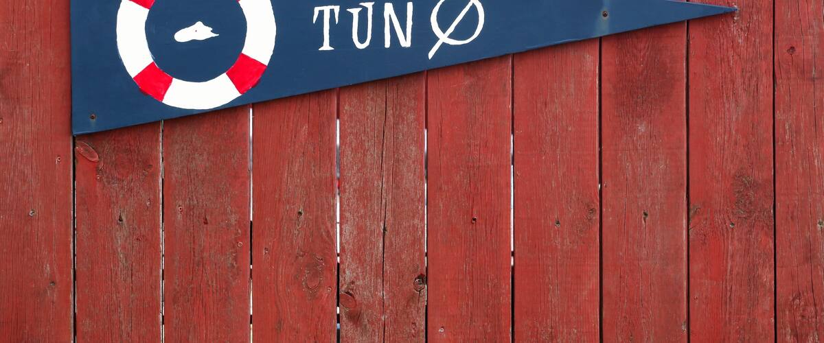 A directional sign with a lifebuoy symbol and the text "TUN Ø" on a blue background, mounted on a red wooden wall.
