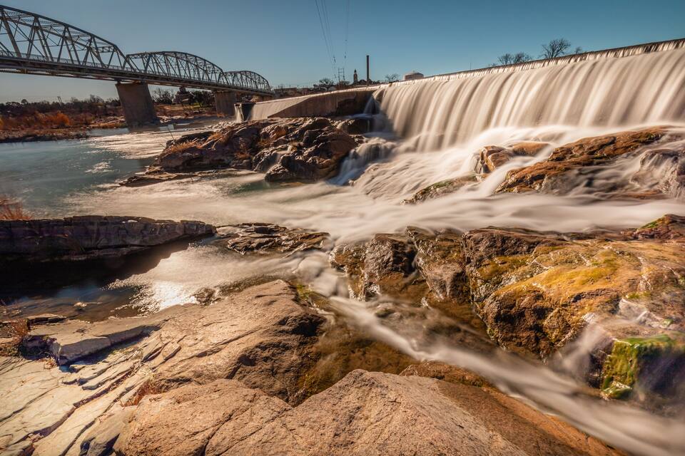 A waterfall cascading over rocks with a bridge in the background.