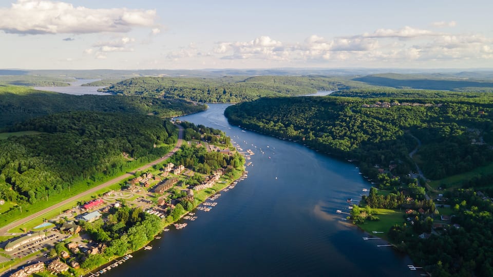 A river winding through a town with boats docked along the shore, surrounded by lush greenery and hills.
