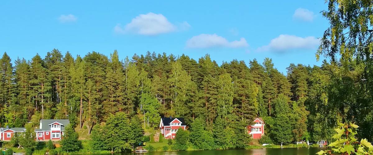 A serene lake with red houses surrounded by dense forest.