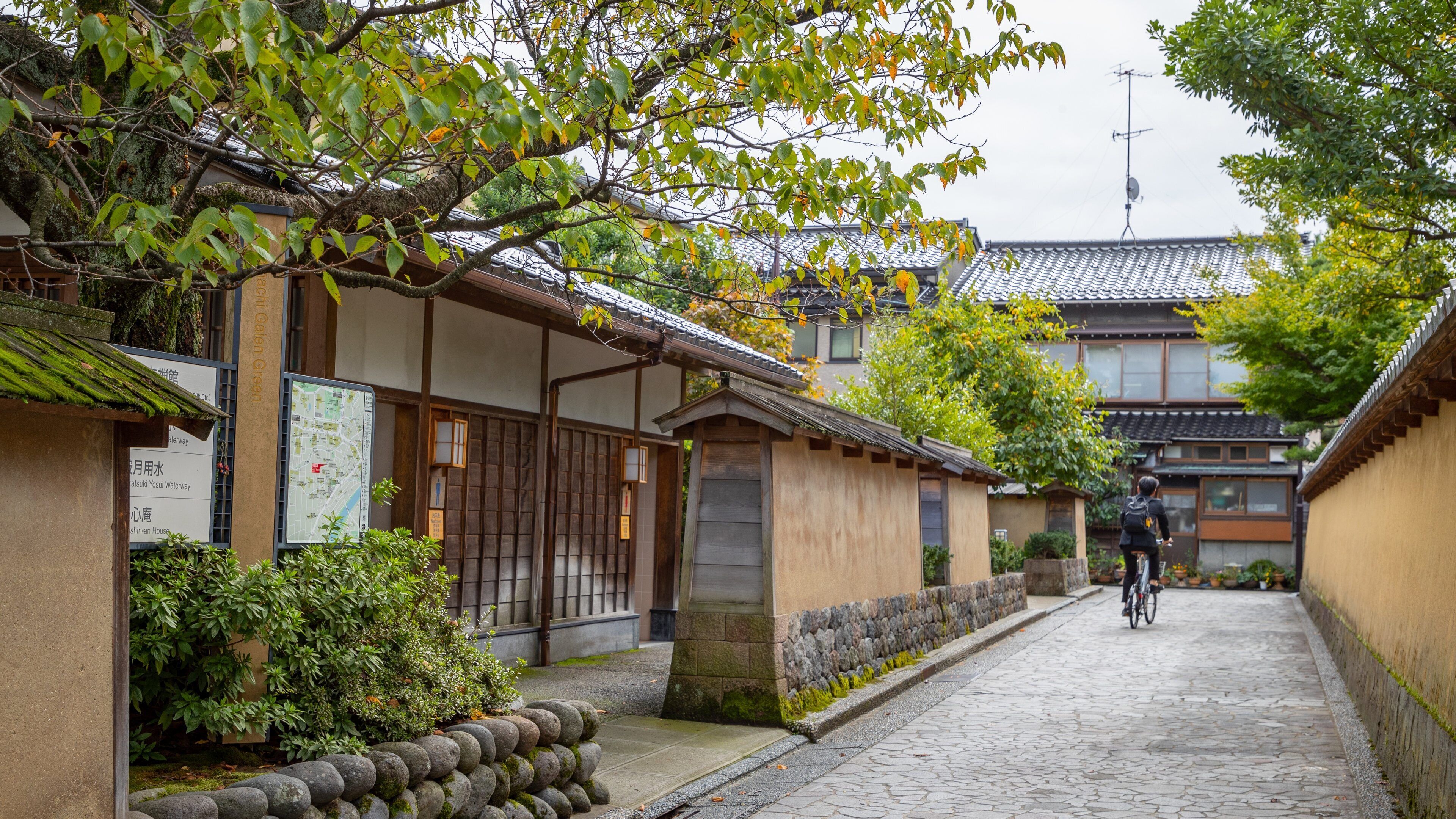 A traditional Japanese street with wooden buildings, stone lanterns, and a cyclist.