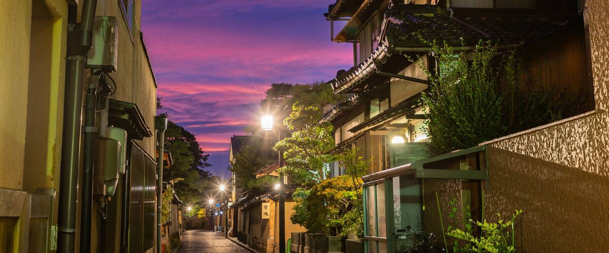 A narrow street at dusk with traditional buildings and a vibrant sunset sky.