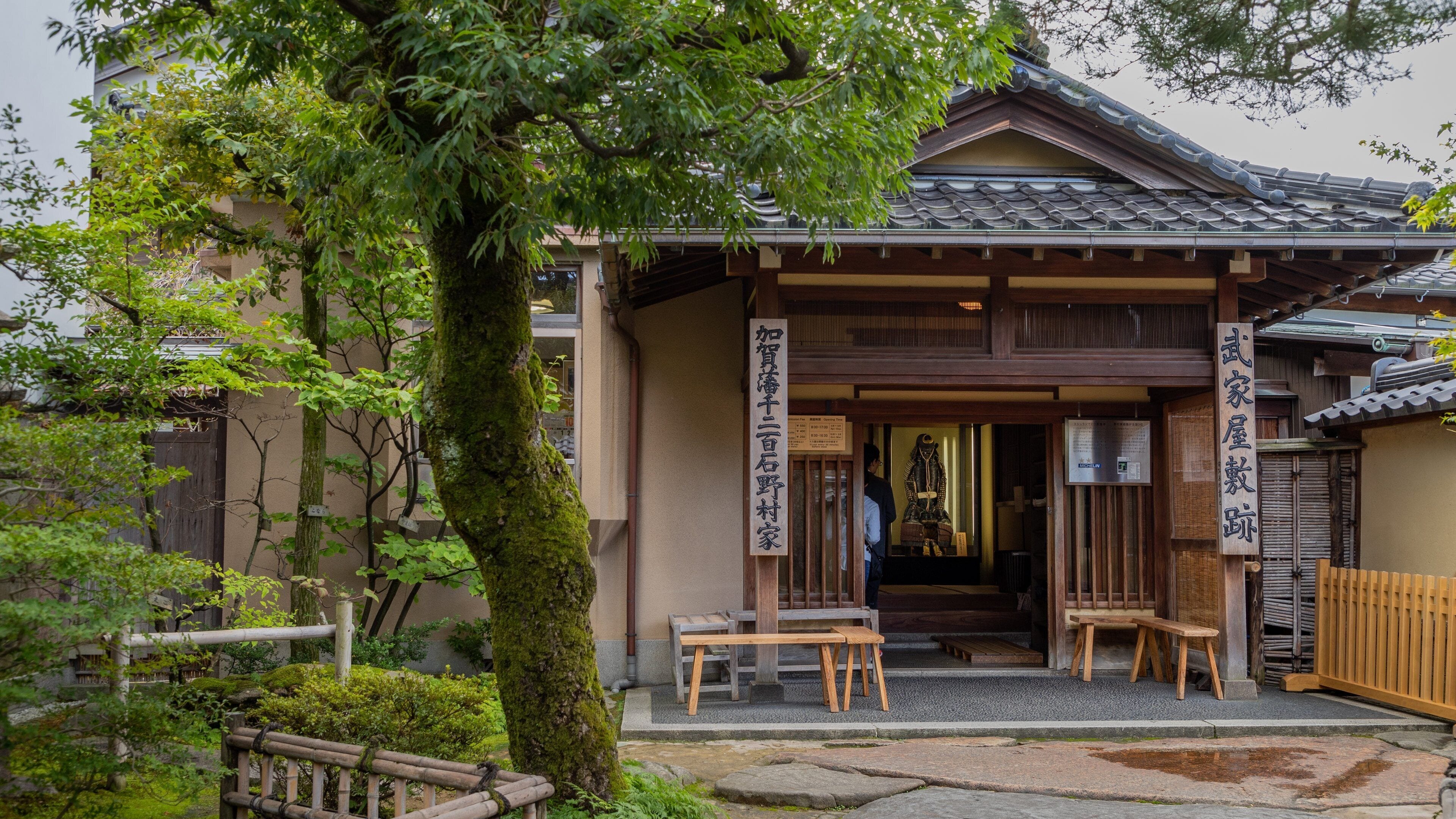 A traditional Japanese house with a tiled roof, wooden beams, and a stone pathway leading to the entrance.
