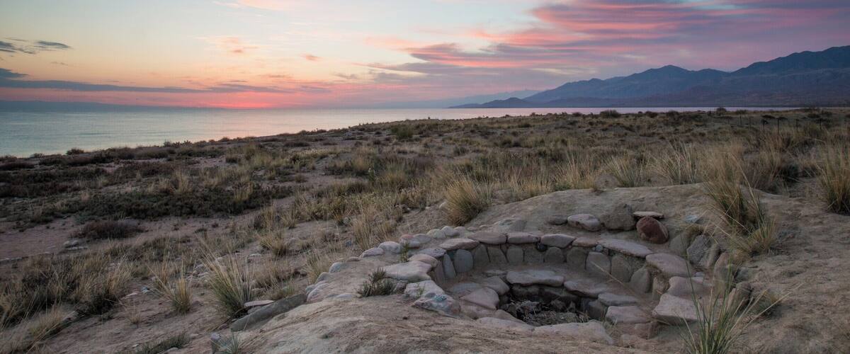 A sunset over a desert landscape with a stone structure in the foreground.