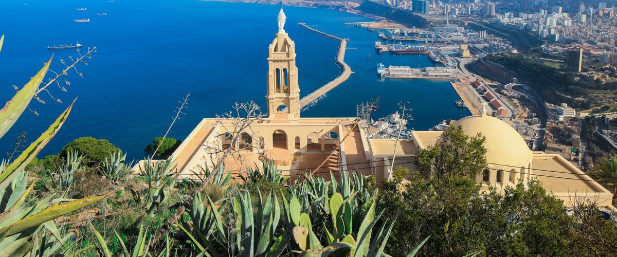A coastal cityscape with a prominent church, a harbor, and a clear blue sea.