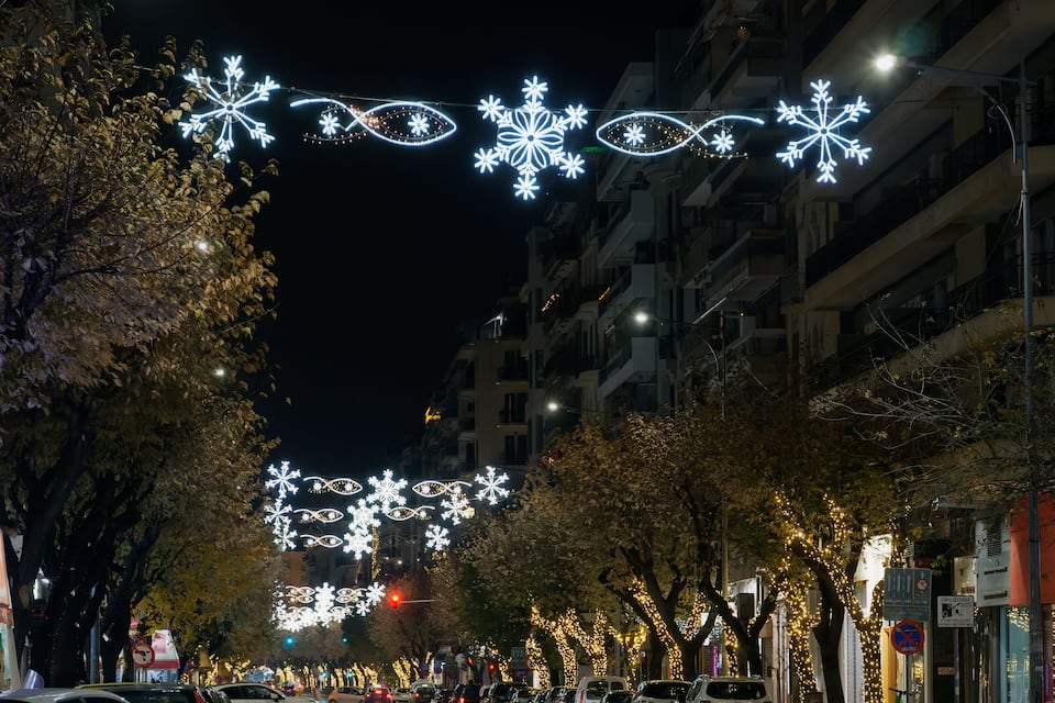 Un carrer de ciutat de nit amb decoracions de flocs de neu il·luminats i arbres.