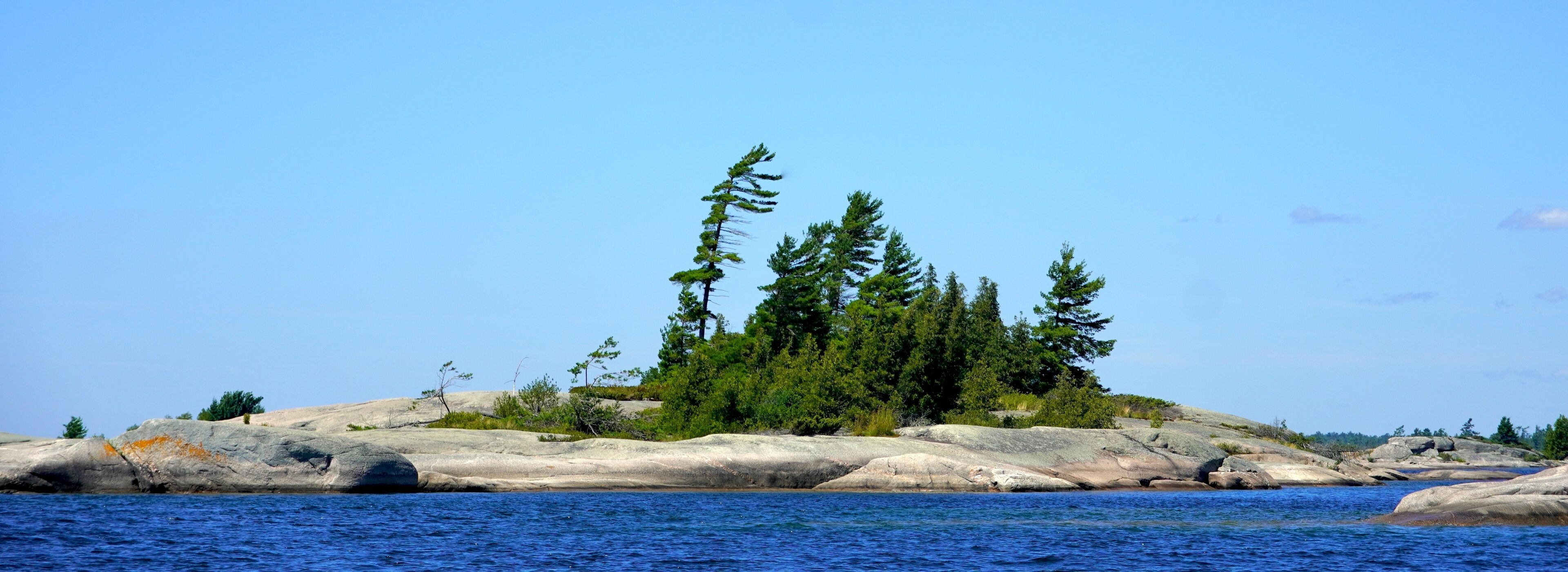 A rocky island with dense green trees and clear blue water.