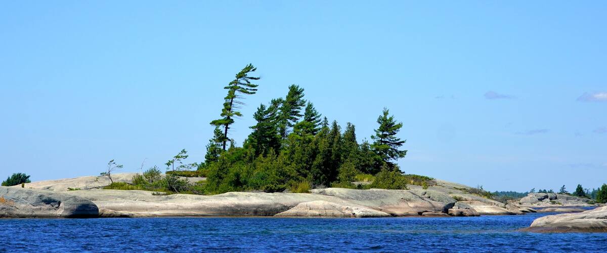 A rocky island with dense green trees and clear blue water.
