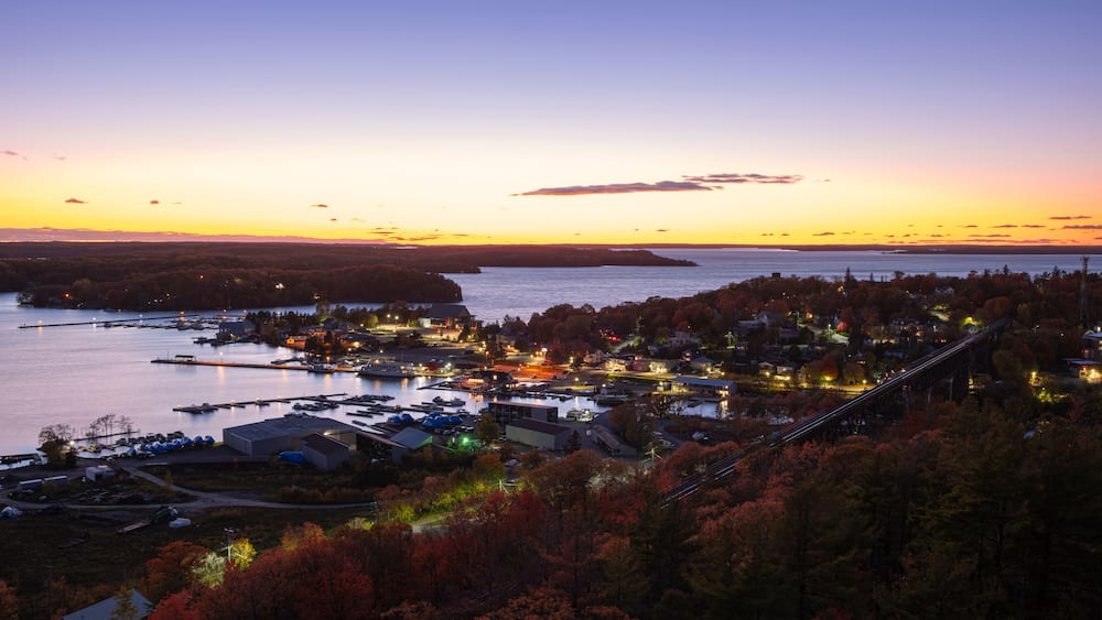 A coastal town at dusk with a bridge, waterfront buildings, and autumn foliage.