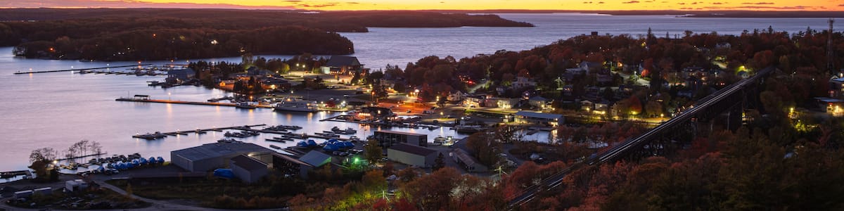 A coastal town at dusk with a bridge, waterfront buildings, and autumn foliage.
