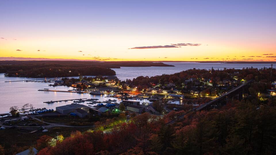 A coastal town at dusk with a bridge, waterfront buildings, and autumn foliage.