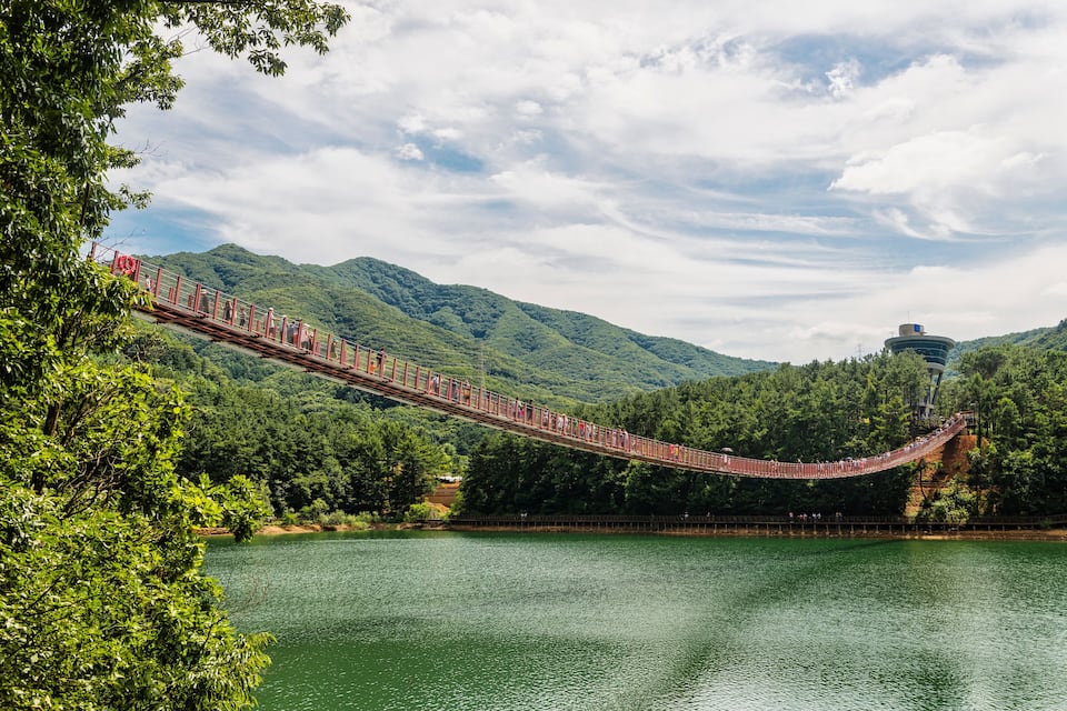 A red suspension bridge over a lake with mountains in the background.