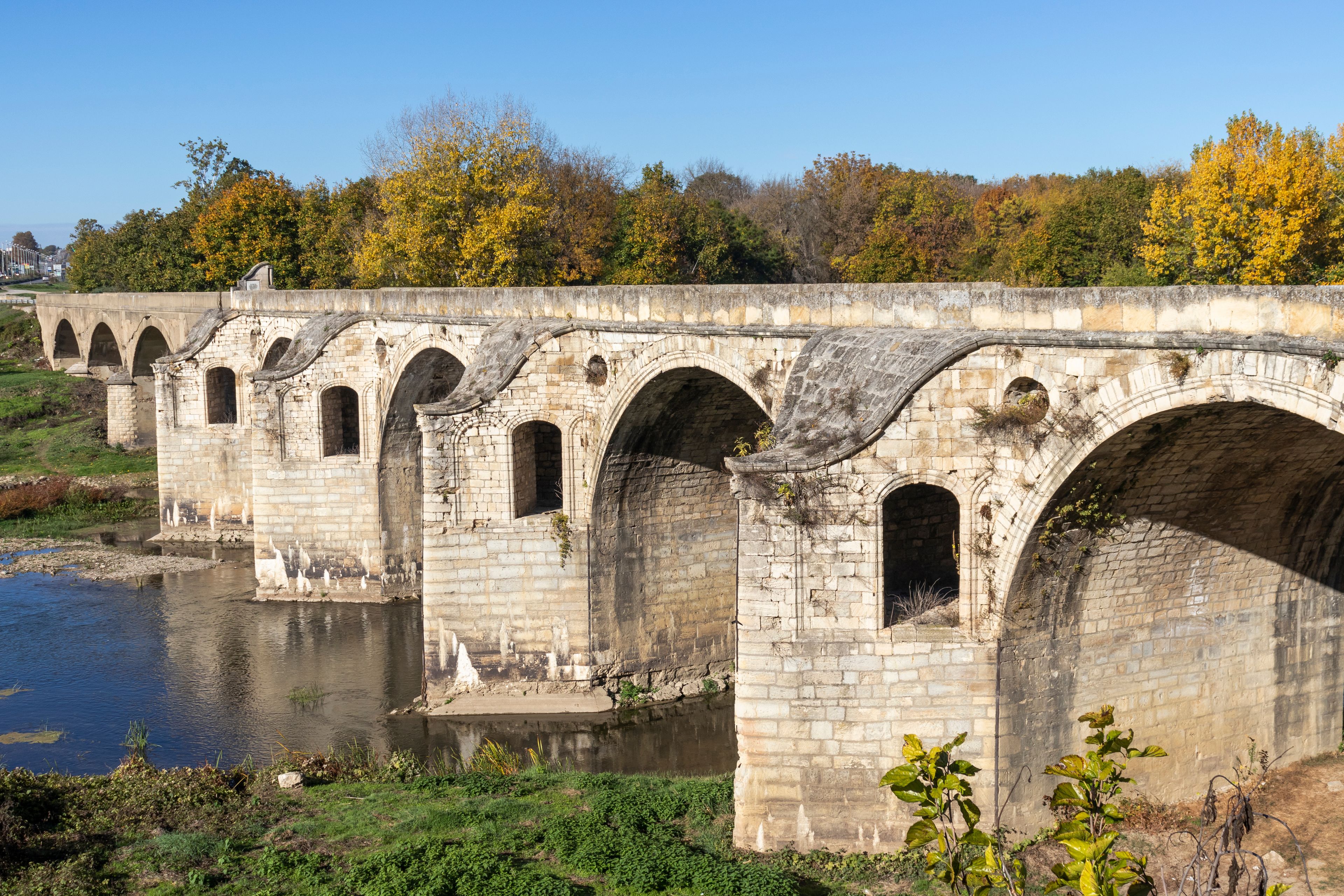 A stone bridge with multiple arches over a river, surrounded by autumn foliage.