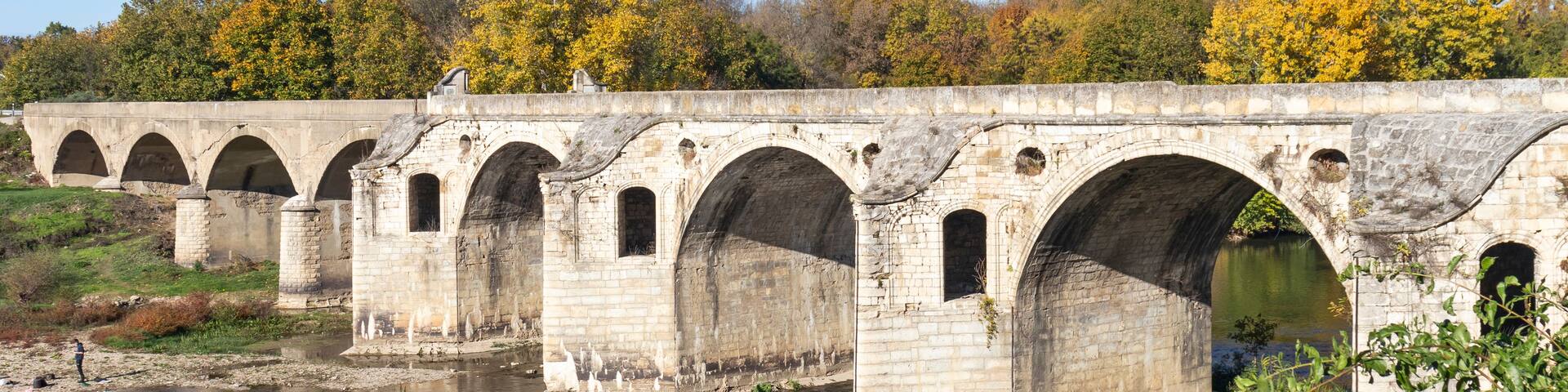 A stone bridge with multiple arches over a river, surrounded by autumn foliage and greenery.
