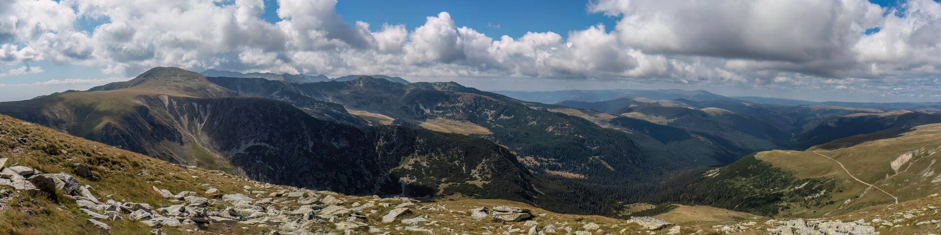 A mountainous landscape with rocky terrain and forested areas under a partly cloudy sky.