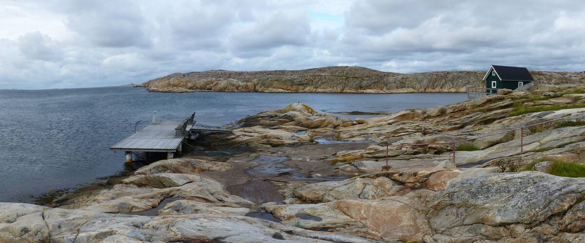 A rocky shoreline with a wooden dock and a green building.