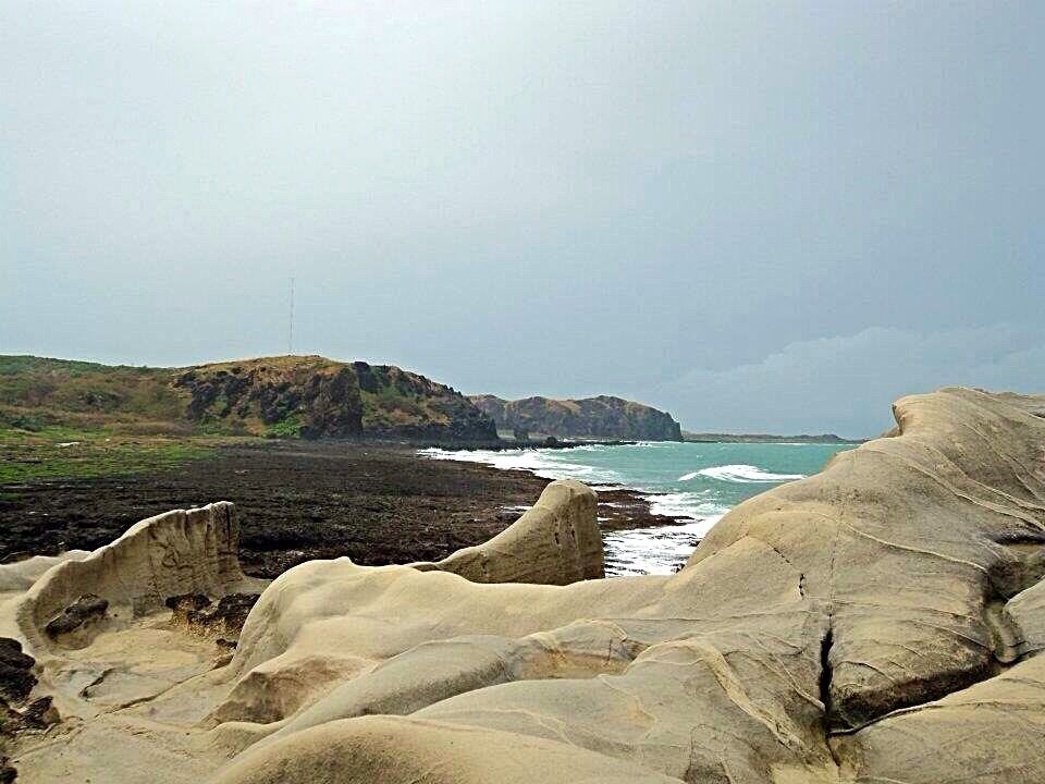 A rocky coastline with waves crashing against the shore and a distant view of cliffs.