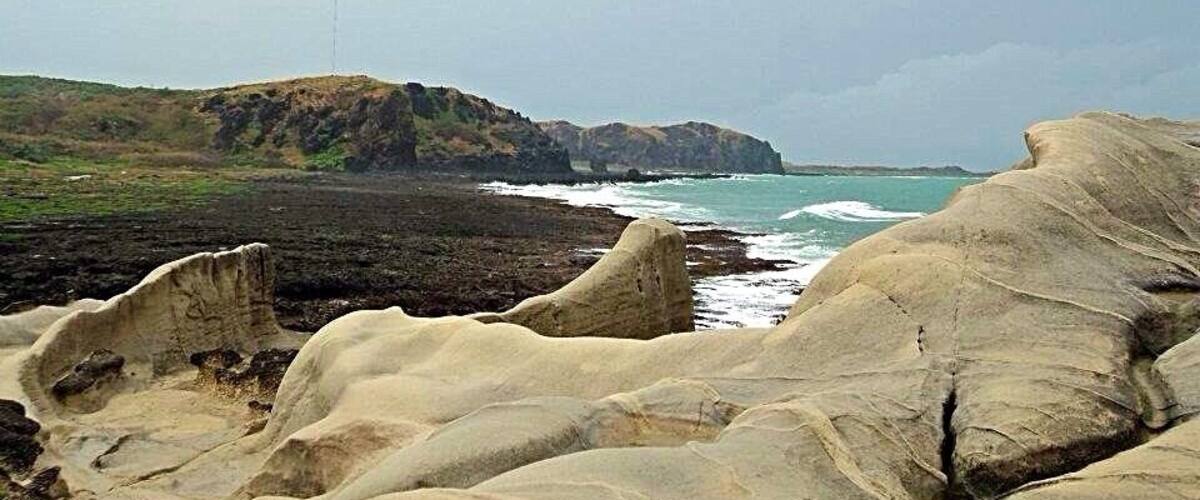A rocky coastline with waves crashing against the shore and a distant view of cliffs.