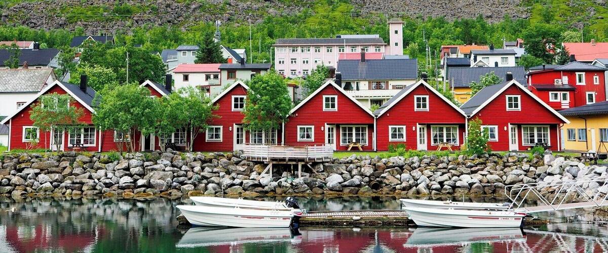 A coastal village with colorful houses, a rocky mountain, and calm water reflecting the buildings.