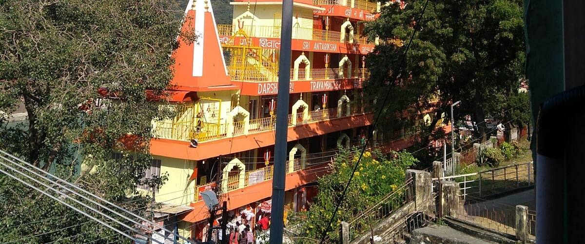 A multi-tiered temple with orange and white colors, surrounded by greenery and hills.