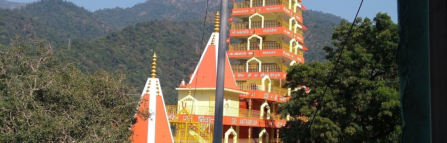 A multi-tiered temple with orange and white colors, surrounded by greenery and hills.