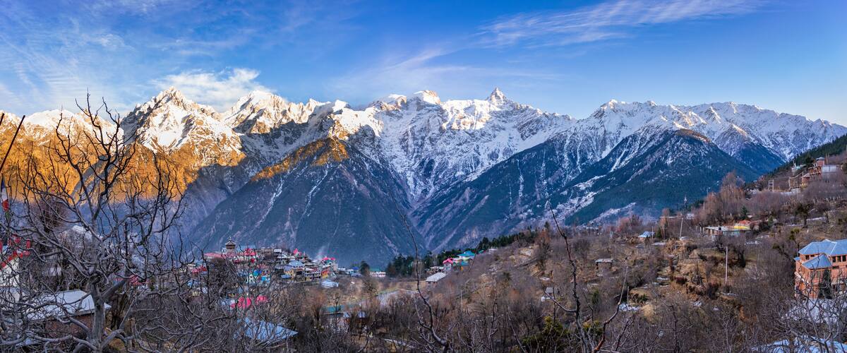 Snow-covered mountains, a village with colorful houses, and a clear blue sky.