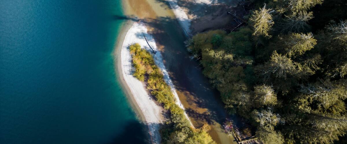An aerial view of a coastal landscape with clear blue waters, a sandy beach, and dense forested areas.