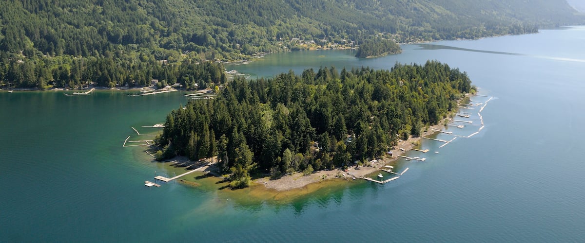 A forested island surrounded by calm water, with mountains in the background.