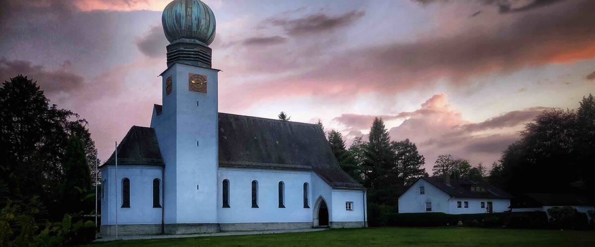 A church with a tall tower and a dome, surrounded by trees and a grassy field.