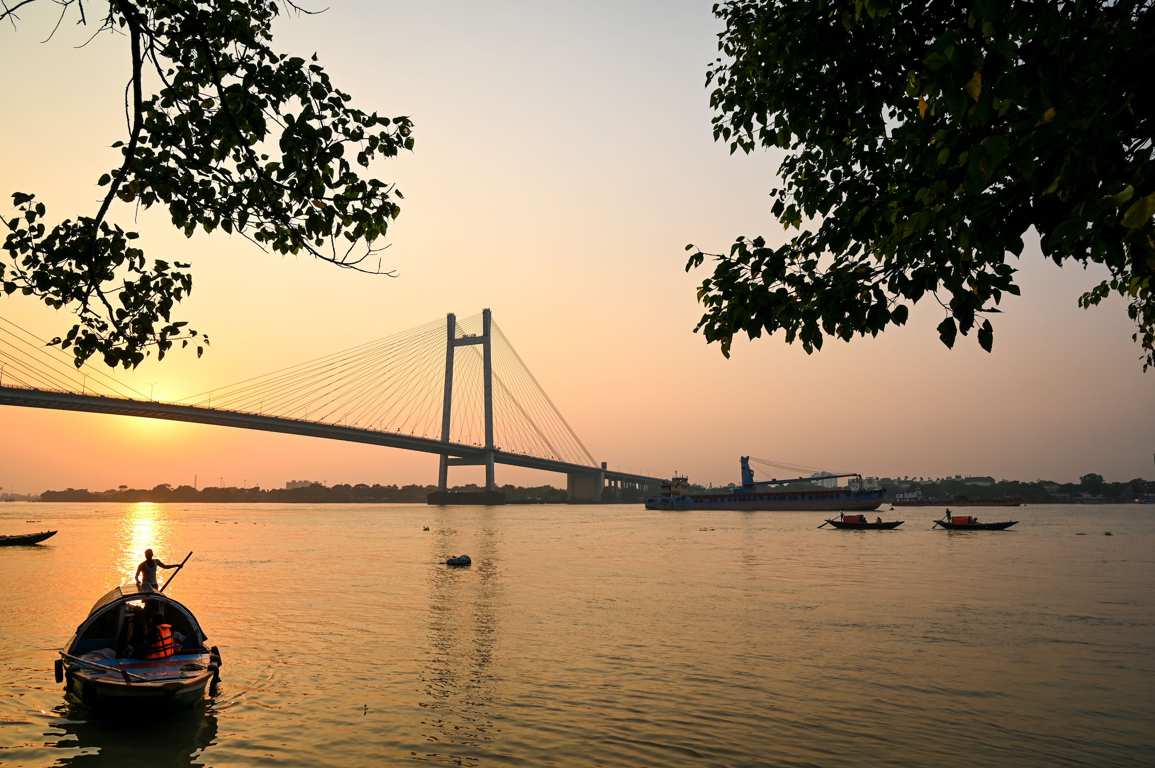 A sunset over a river with a bridge and boats.