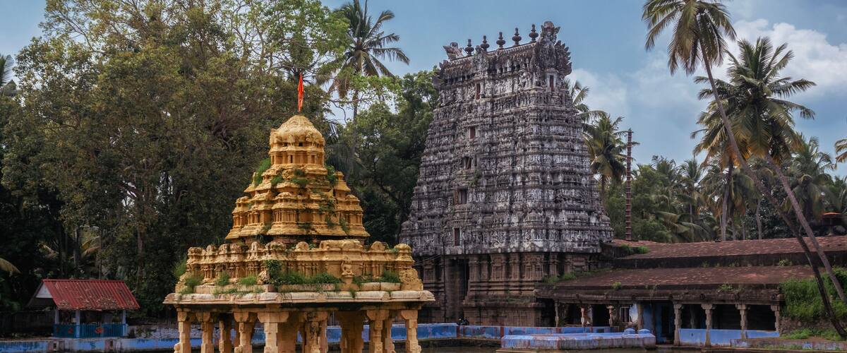 A temple with intricate carvings and a large stone structure in a serene lake setting.