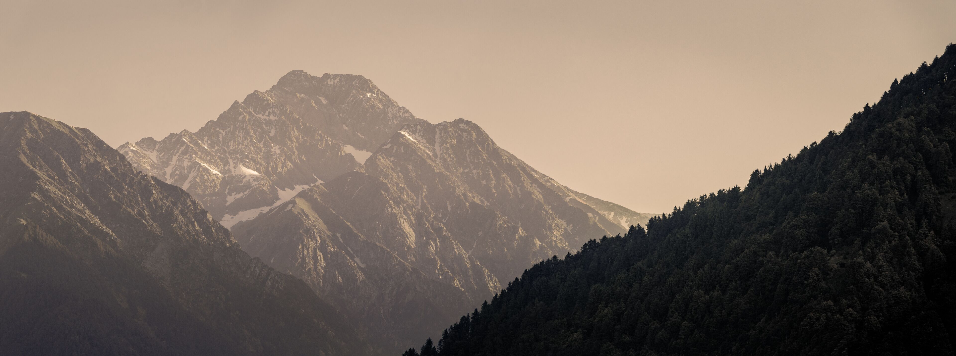 A mountain range with snow-capped peaks and dense forested slopes.