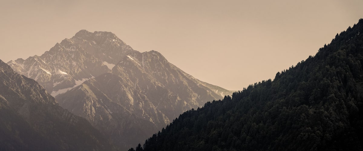 A mountain range with snow-capped peaks and dense forested slopes.