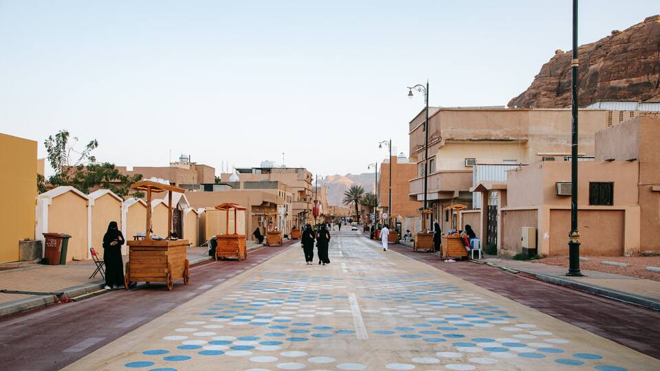 A street with buildings, a patterned road, and a mountain in the background.